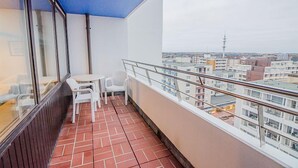 A balcony with a tiled floor, a small table with chairs, and a view of a cityscape with buildings and a tower. - House Sylter Welle 8-87, OB (Sylt/Westerland)