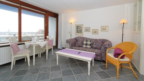 En hyggelig stue med en sofa, et spisebord med stole, et sofabord og udsigt over byen gennem store vinduer.
