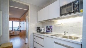 Cocina compacta con armarios blancos, microondas, cafetera y lavamanos.