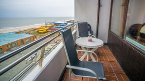 Un balcón con vista a la playa y toboganes acuáticos, una mesa con una bebida y dos sillas.