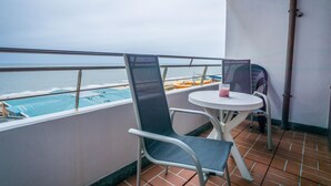 Un balcón con dos sillas y una mesa, con vista a una piscina y al mar.