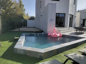 Relax by the serene pool surrounded by lush greenery and a clean, modern building.