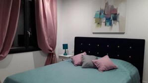 Un dormitori amb un llit, una tauleta de nit, una làmpada i una obra d'art a la paret.