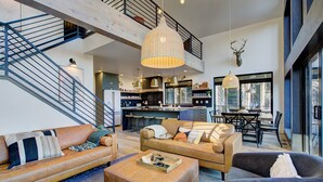 Un amplio salón con techo alto, una escalera y una cocina al fondo.