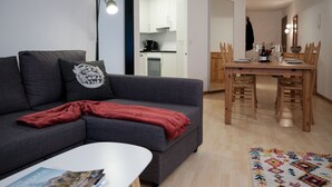 Een moderne woonkamer met een grijze bank, een rode plaid, een witte salontafel en een eethoek met een houten tafel en stoelen.
