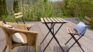 Una terraza en la azotea con sillas de mimbre, una mesa de madera y vistas a un edificio con tejado de tejas.