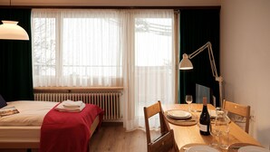 A hotel room with a bed, a wooden dining table set for two, and a window with sheer curtains. - Silence by Interhome (Zermatt)