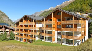 A multi-story wooden building with balconies, set against a mountainous backdrop. - Silence by Interhome (Zermatt)