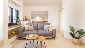 A modern living room with a grey sofa, two round tables, and a kitchen in the background. - Antigoni's Seaside Lodge (Rethymno)