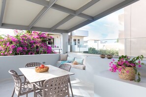 An outdoor seating area with a table and chairs, surrounded by vibrant pink flowers and a view of the city. - Antigoni's Seaside Lodge (Rethymno)