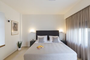 A neatly arranged hotel room with a large bed, two bedside tables, a potted plant, and a framed picture on the wall. - Antigoni's Seaside Lodge (Rethymno)