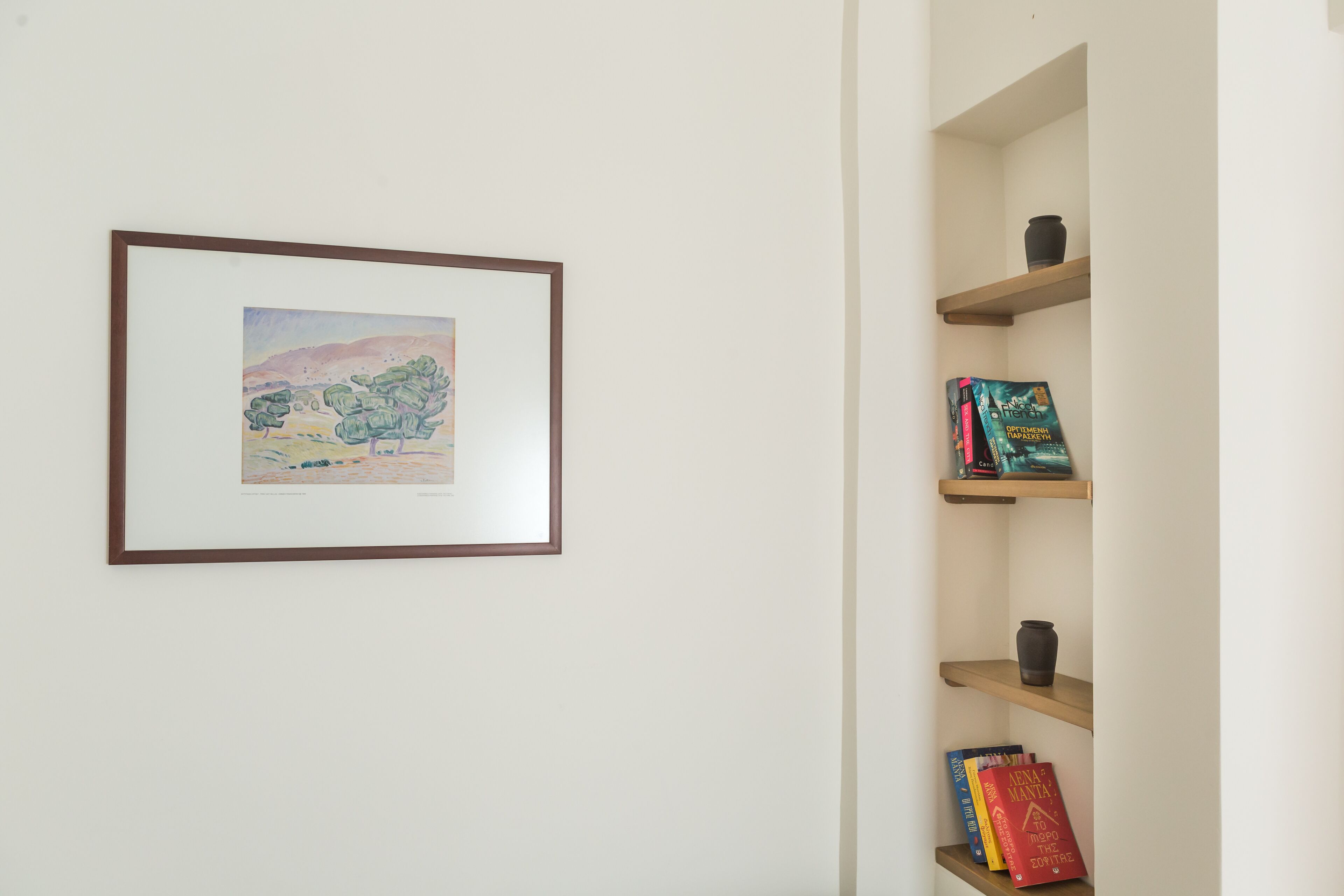 A framed painting on a wall, a bookshelf with books and decorative items, and a small shelf with a vase.