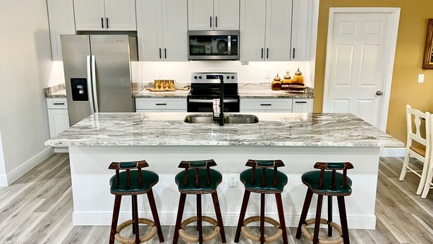 A kitchen with a central island, stainless steel appliances, and bar stools.