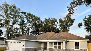 A single-story house with a garage, stone foundation, and a sloped roof.