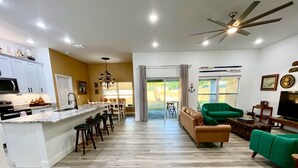 A spacious living area with a kitchen, a dining area, and a seating area with green sofas.