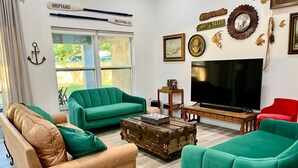A living room with green sofas, a wooden coffee table, and a large flat-screen TV.