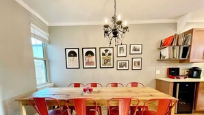 A dining area with a wooden table and red chairs, a chandelier, framed pictures on the wall, and a kitchen area with a microwave and bookshelves. - Larry's Lancaster Landing: 3 bedroom row house, walkable to downtown Lancaster (Lancaster)