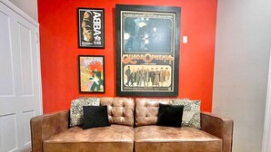 A brown leather sofa with black and patterned cushions against a red wall, with movie posters above. - Larry's Lancaster Landing: 3 bedroom row house, walkable to downtown Lancaster (Lancaster)