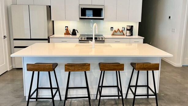 A modern kitchen with white cabinetry, a central island with bar stools, a microwave, and a coffee maker. - The Butterfly House: with sauna and fully-fenced yard  (Sanford)