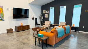 A modern living room with a large flat-screen TV, a sofa, chairs, and a wooden cabinet. - The Butterfly House: with sauna and fully-fenced yard  (Sanford)