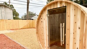 A wooden sauna with a glass door, a gravel path, and a wooden fence in the background. - The Butterfly House: with sauna and fully-fenced yard  (Sanford)