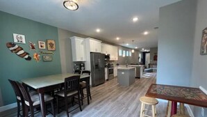 A modern kitchen with white cabinets, a central island, and a dining area with wooden chairs. - The Billiard: super fun home close to downtown with fully-fenced yard (Sanford)