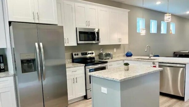 A modern kitchen with stainless steel appliances, white cabinetry, and a central island. - The Billiard: super fun home close to downtown with fully-fenced yard (Sanford)