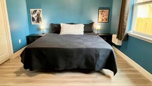 A bedroom with a large bed, two bedside tables with lamps, and artwork on the walls. - The Billiard: super fun home close to downtown with fully-fenced yard (Sanford)