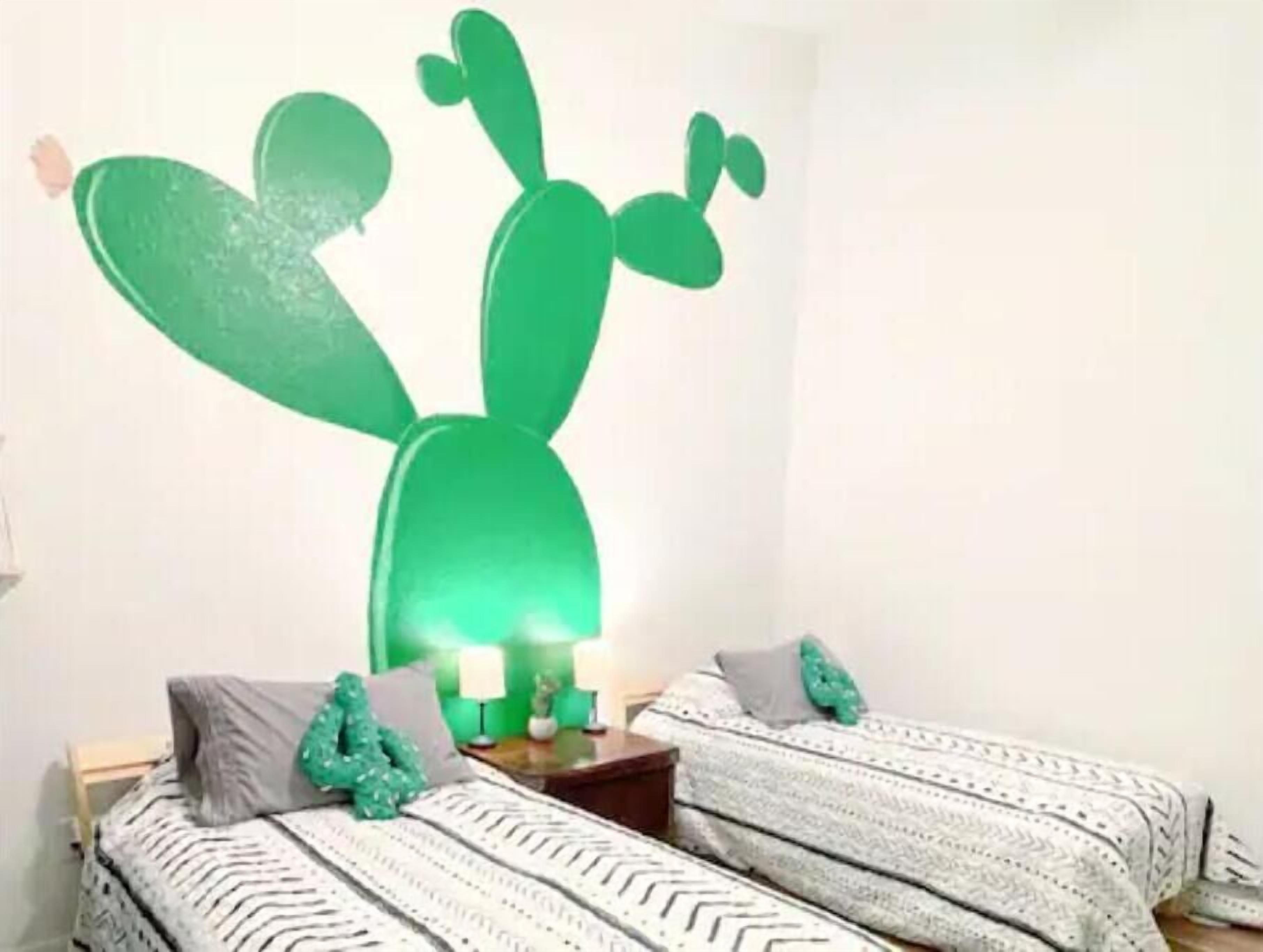 A room with two beds, a cactus wall art, and a nightstand with candles.