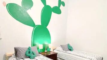 A room with two beds, a cactus wall art, and a nightstand with candles.