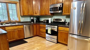 A kitchen with wooden cabinets, stainless steel appliances, a dishwasher, and a window with a view of trees.