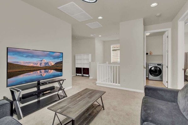 A modern living room with a flat-screen TV, a wooden coffee table, and grey sofas.