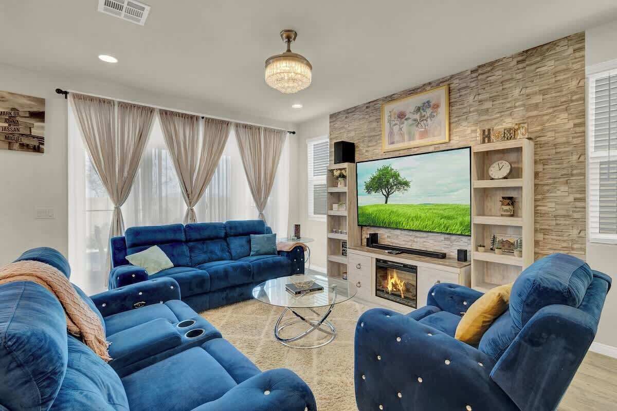 A modern living room with a blue sofa set, a glass coffee table, a flat-screen TV, and a fireplace.