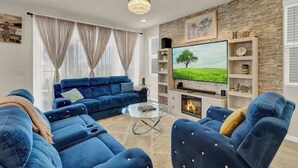A modern living room with a blue sofa set, a glass coffee table, a flat-screen TV, and a fireplace.