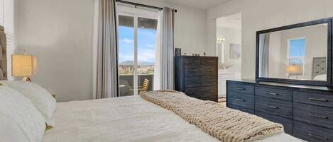 A bedroom with a large bed, a dresser, a mirror, and a view through a sliding door.