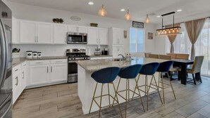 A modern kitchen with white cabinets, a central island with bar stools, stainless steel appliances, and pendant lighting.