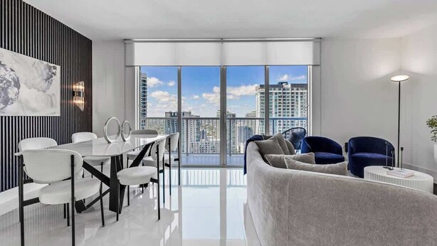 A modern living room with a dining area, large windows, and a view of the cityscape.