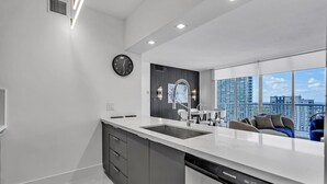 A modern kitchen with a large island, a built-in dishwasher, and a view of the cityscape through large windows.