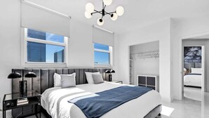 A modern bedroom with a large bed, bedside tables, a wardrobe, and a view of the city.