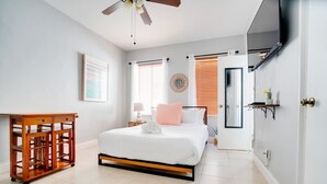 A bedroom with a bed, a wooden side table, a ceiling fan, a large mirror, and a door leading to another room. - Comfy Studio with Beach Access across the street (Miami)