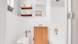 A compact bathroom with a white toilet, a wooden cabinet, and a small shelf with toiletries. - Comfy Studio with Beach Access across the street (Miami)