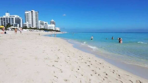 A beach with clear blue water, sandy shore, and high-rise buildings in the background. - Comfy Studio with Beach Access across the street (Miami)