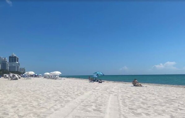 A beach with tents and umbrellas, a clear sky, and a calm sea.