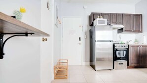 A modern kitchen with stainless steel appliances, wooden cabinets, and a white tiled floor. - Comfy Studio with Beach Access across the street (Miami)