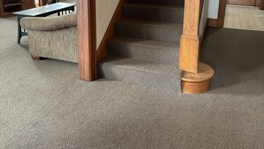 A carpeted staircase with wooden railings, a television on a stand, and a dining area with a table and chairs.
