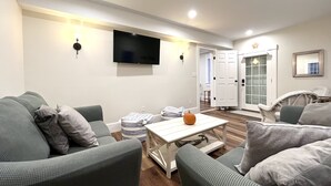 A living room with a flat-screen TV mounted on the wall, a white coffee table, and two green sofas with cushions. - Historical charm | Modern amenities | Unbeatable location (Ogunquit)