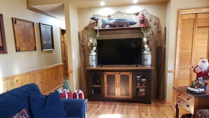A living room with a blue sofa, wooden flooring, a TV on a wooden cabinet, and Christmas decorations. - Adorable, cozy, waterfront cabin on the River, fish, kayak, tube from property. (Mineral Bluff)