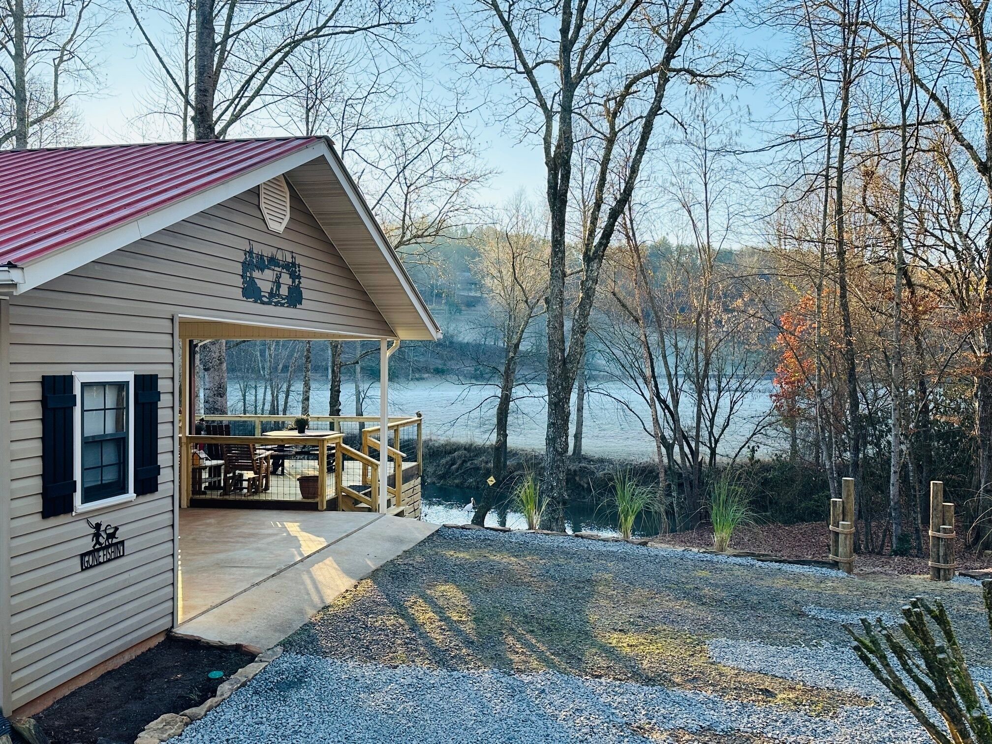 Une cabane dotée d’un porche abrité, d’un coin repas et offrant une vue sur un lac entouré d’arbres.