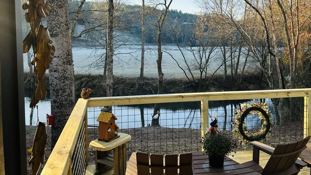 A wooden deck with a view of a lake, surrounded by trees. - Adorable, cozy, waterfront cabin on the River, fish, kayak, tube from property. (Mineral Bluff)