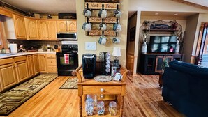A cozy kitchen with wooden cabinets, a coffee sign, and a coffee maker on a wooden table. - Adorable, cozy, waterfront cabin on the River, fish, kayak, tube from property. (Mineral Bluff)